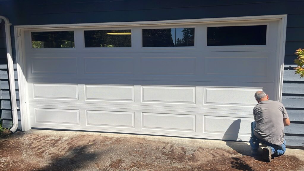 Technician finishing a newly installed white insulated garage door with a top row of windows