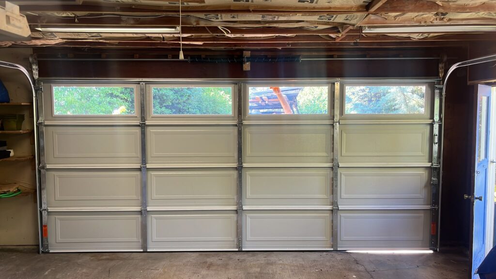 Newly installed garage door panels with windows, tracks and rollers viewed from inside the garage
